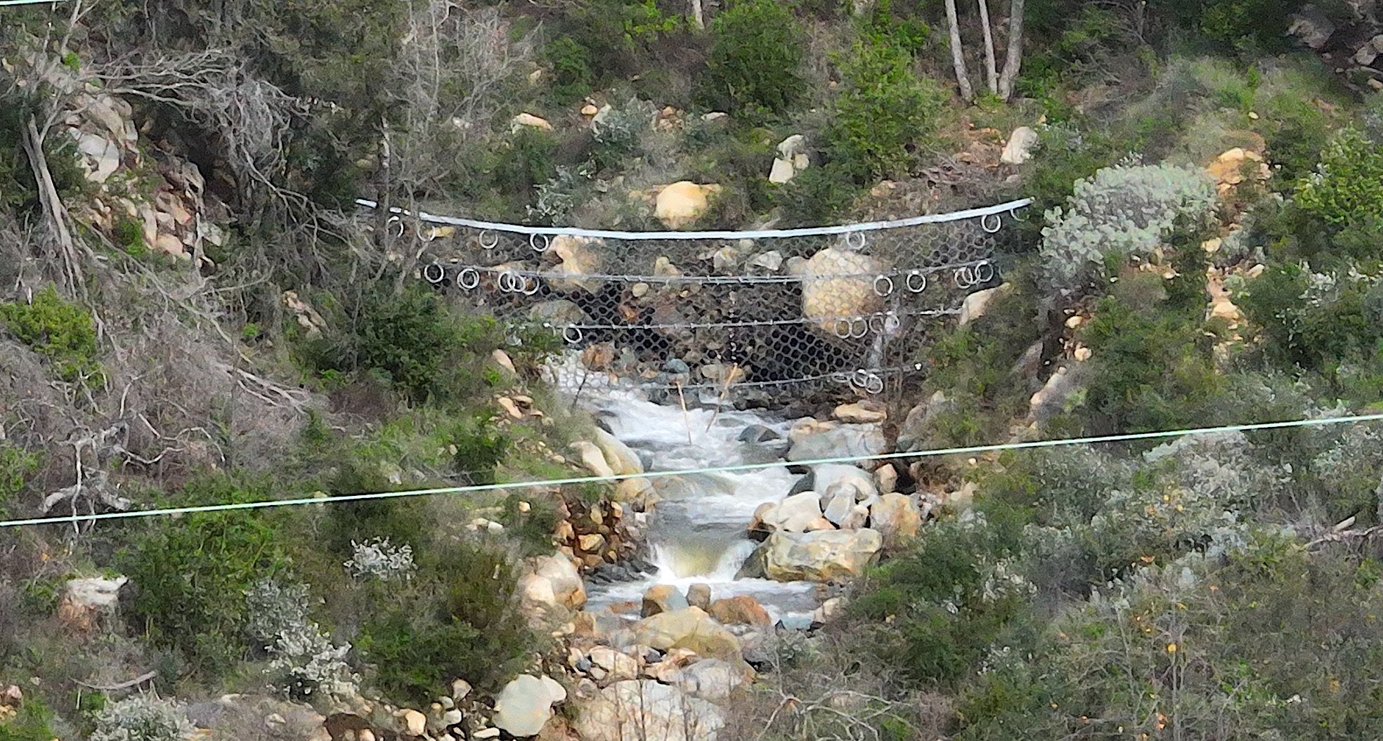 Steel mesh nets strung above a Santa Barbara County creek, with white water flowing in the creek bed